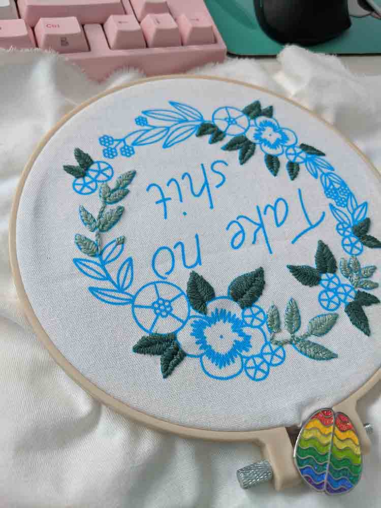Floral wreath with dark green and light green leaves embroidered. The rest is outlined in blue.
