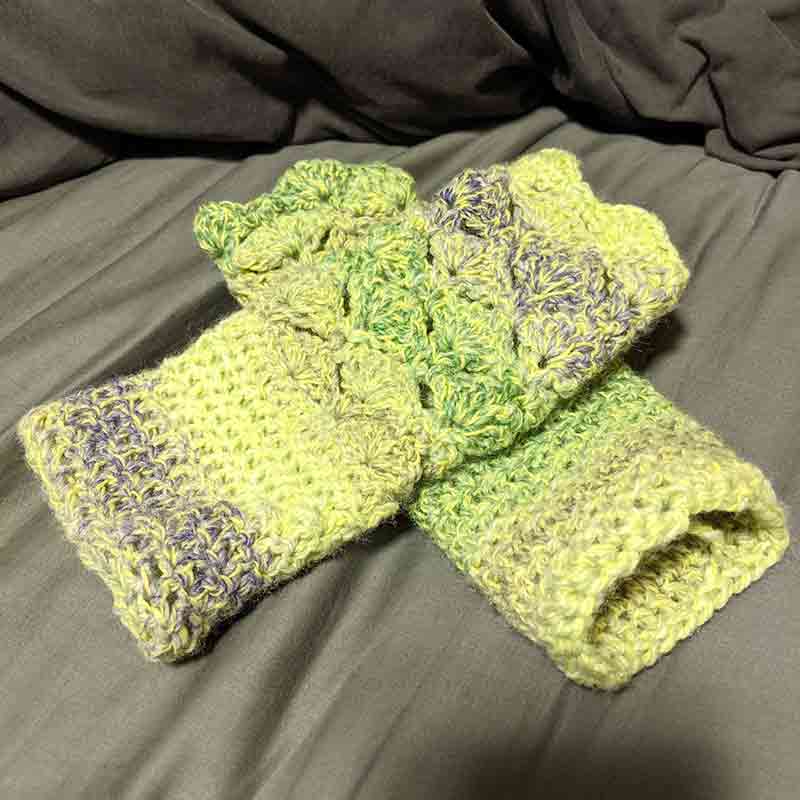 Crocheted fingerless gloves made from green and purple marbled yarn.
