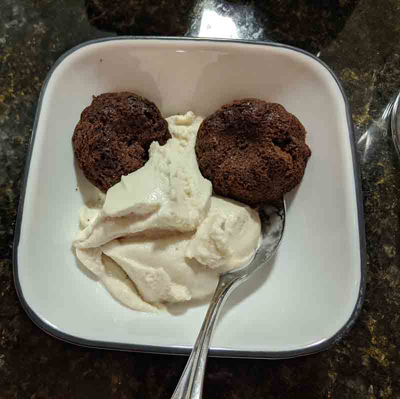 Bowl of two brownies with light tan ice cream.