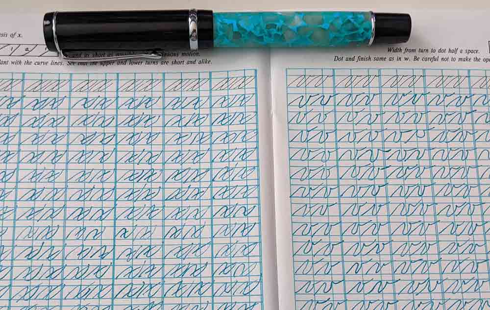 Teal fountain pen at the top of a handwriting workbook.