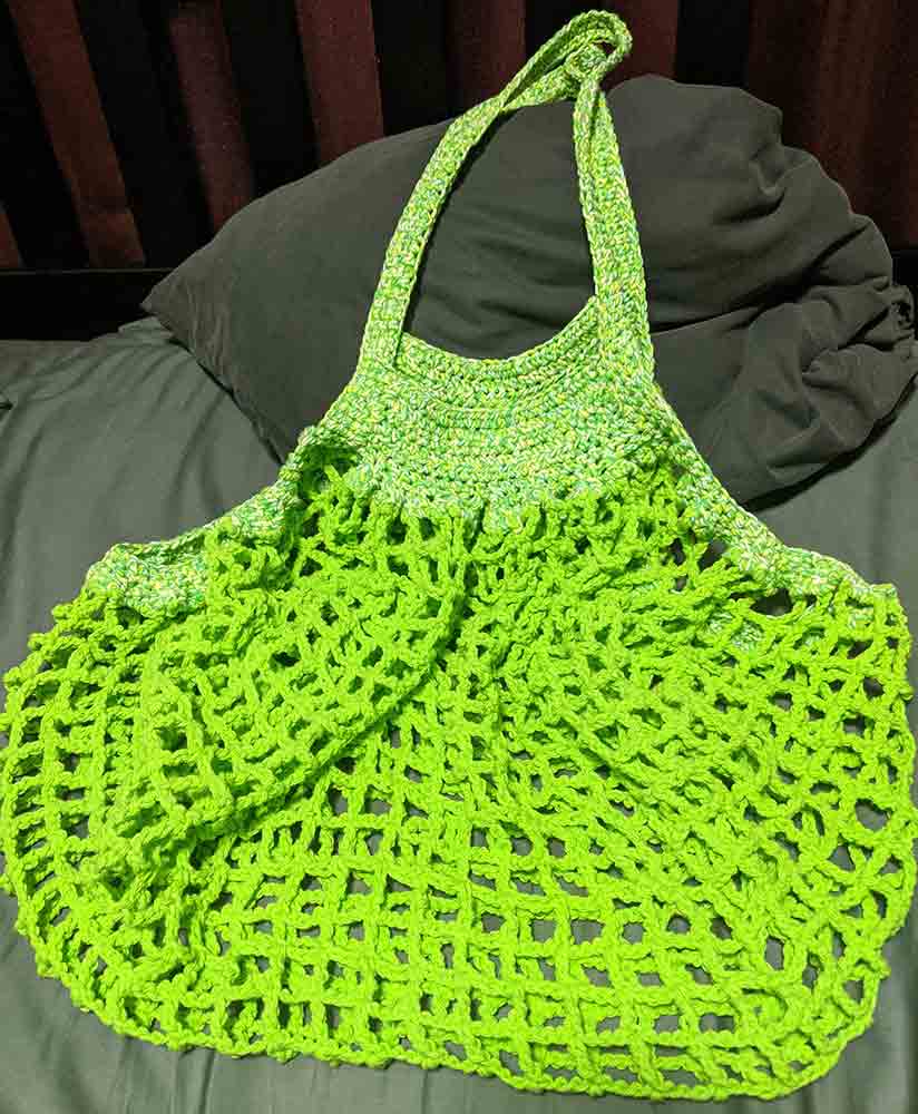 Green crocheted bag lying on a bed.