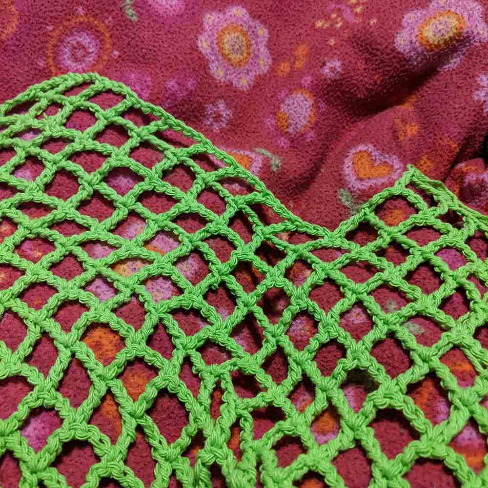 Lime green yarn crocheted in a net pattern on a bright pink blanket. The crochet net is missing quite a few stitches on the third row from the top, the other two rows skipped them as well.