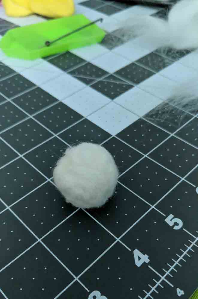 Small white ball of wool on a grey cutting mat.