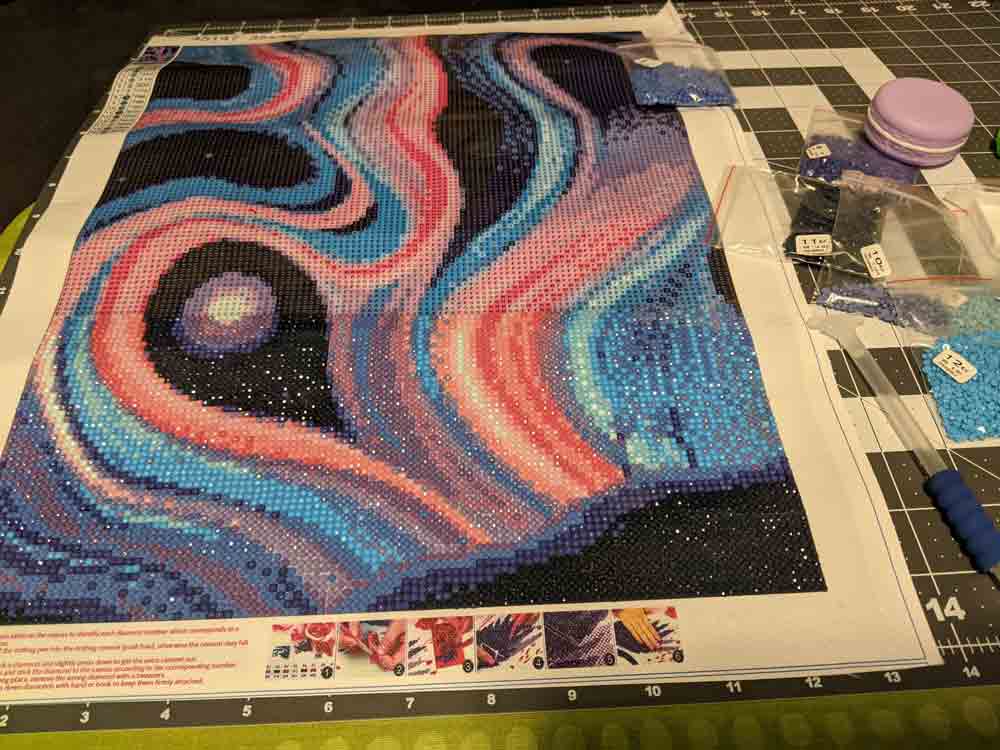 Purple, blue, and pink swirls diamond painting that is about a third complete.